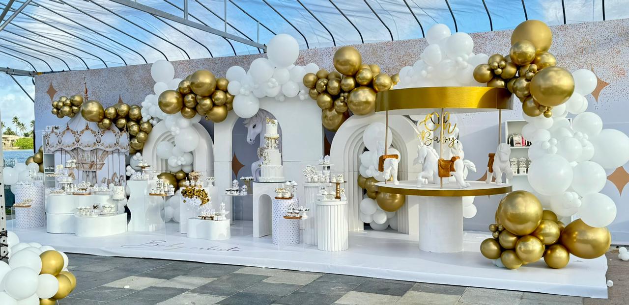 Decoração para chá revelação nas cores branco e dourado, tema carrossel. Arcos, balões, e mesas, em ambiente aberto 