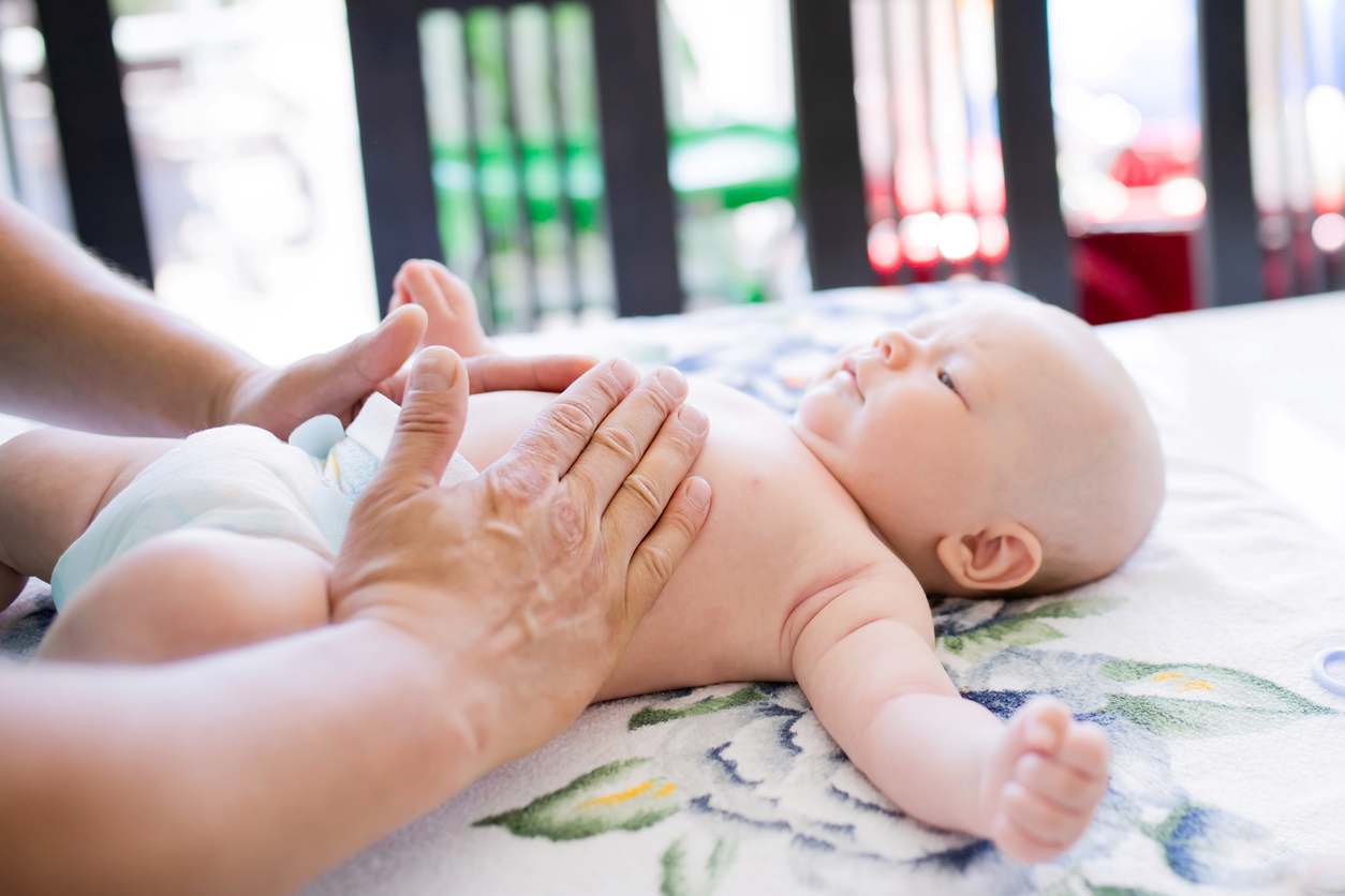 Bebê deitado de barriguinha para cima, sendo massageado por seu cuidador.
