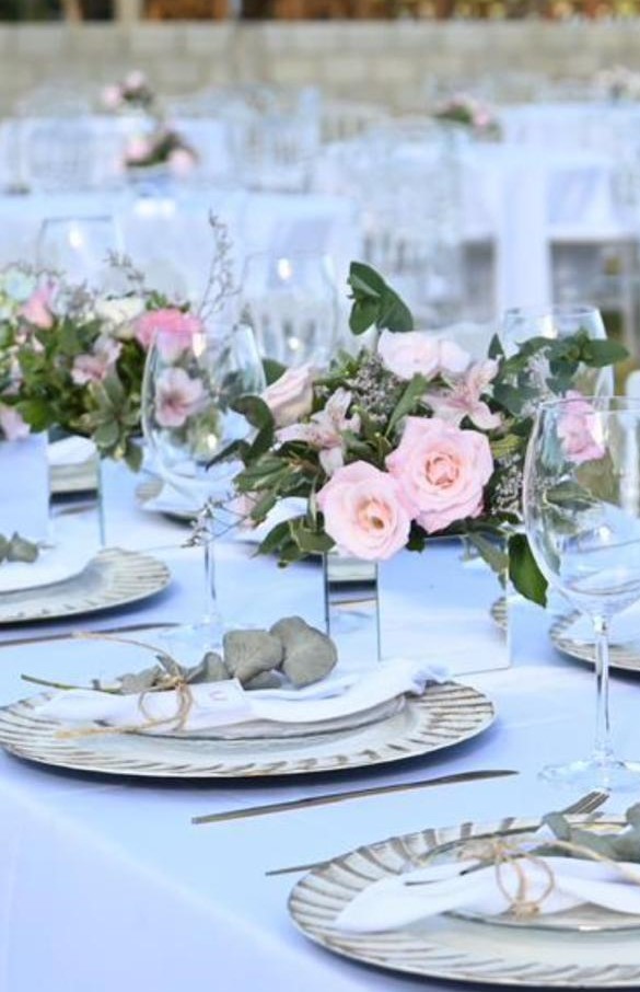 Mesa refinada posta com decoração para chá revelação. Pratos, talheres e vasos de espelho com buquês de rosas cor de rosa bebê 