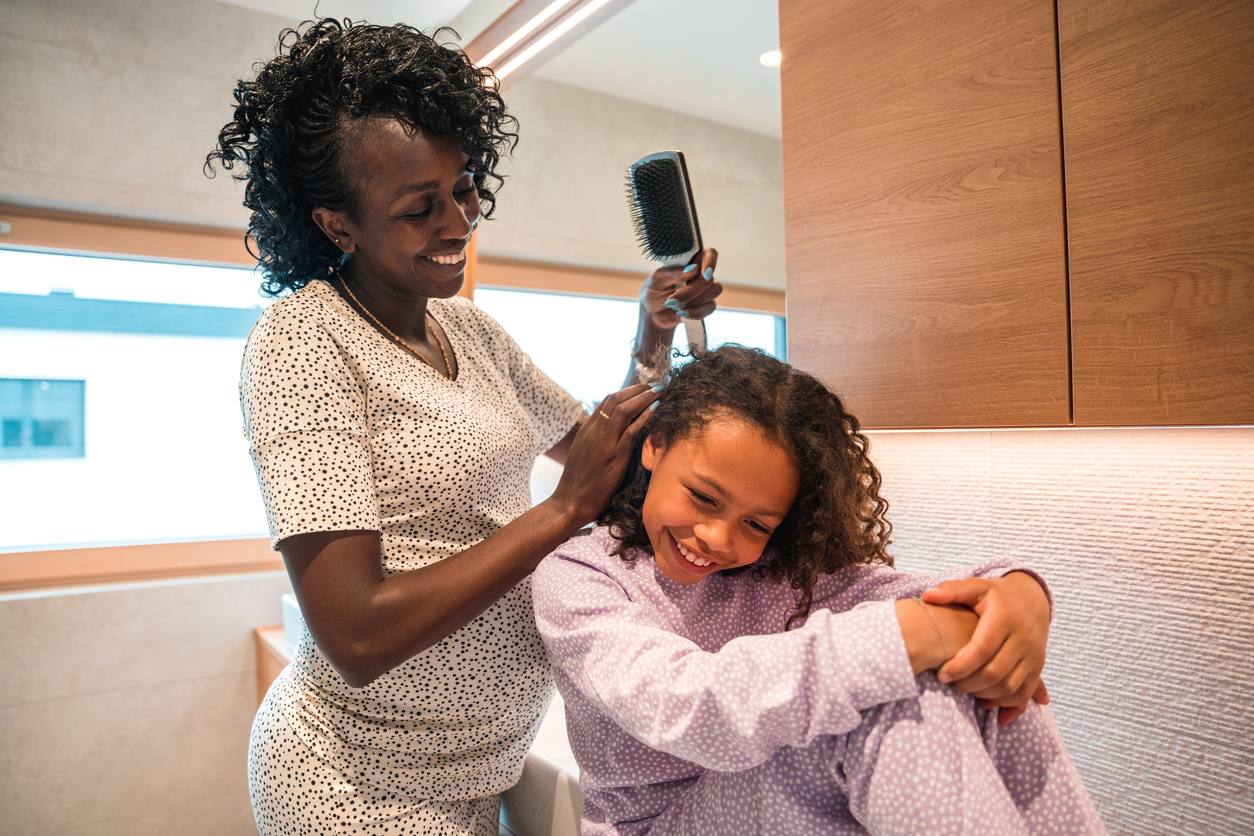 Mãe penteando o cabelo de sua filha, cheio de cachinhos.