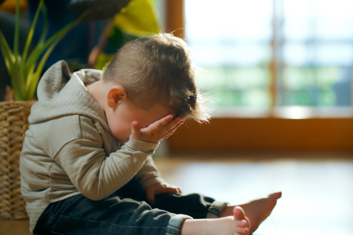 Criança pequena chorando com as mãos no rosto sentado no chão