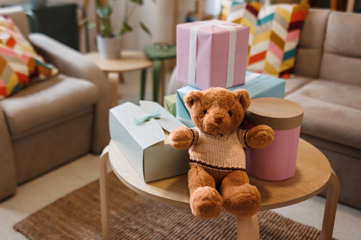 Mesinha com caixas de presente e urso de pelúcia em chá de bebê simples. O ambiente é a sala de uma casa com iluminação natural 