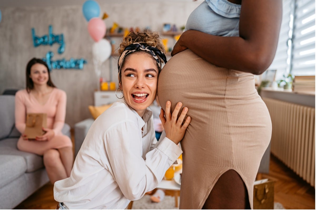 Mulher ouvindo barriga de gestante durante cha de bebe